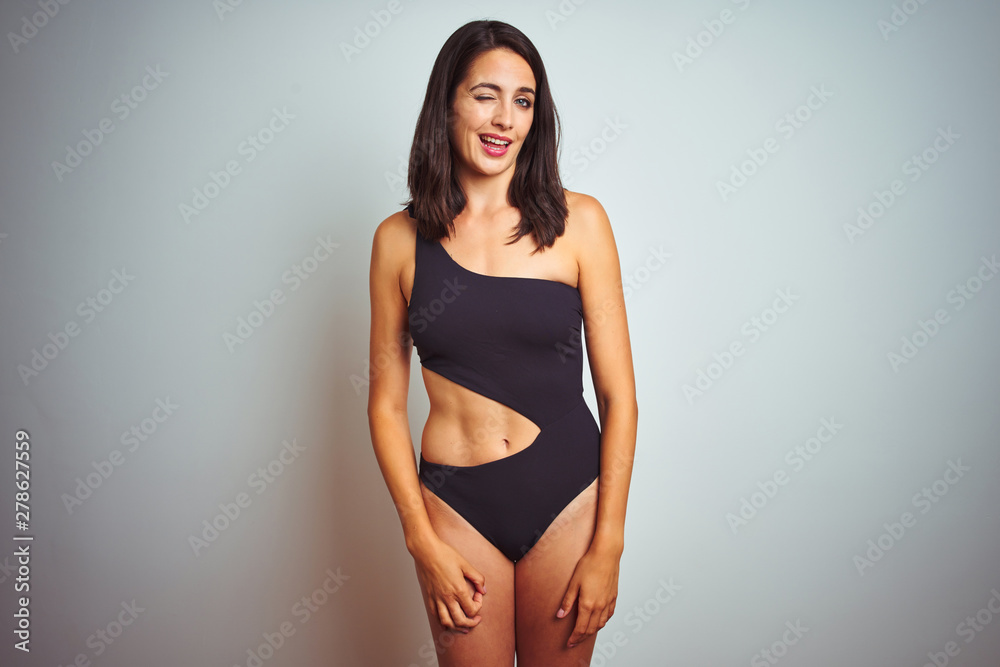 Beautiful woman wearing bikini swimwear over white isolated background winking looking at the camera with sexy expression, cheerful and happy face.