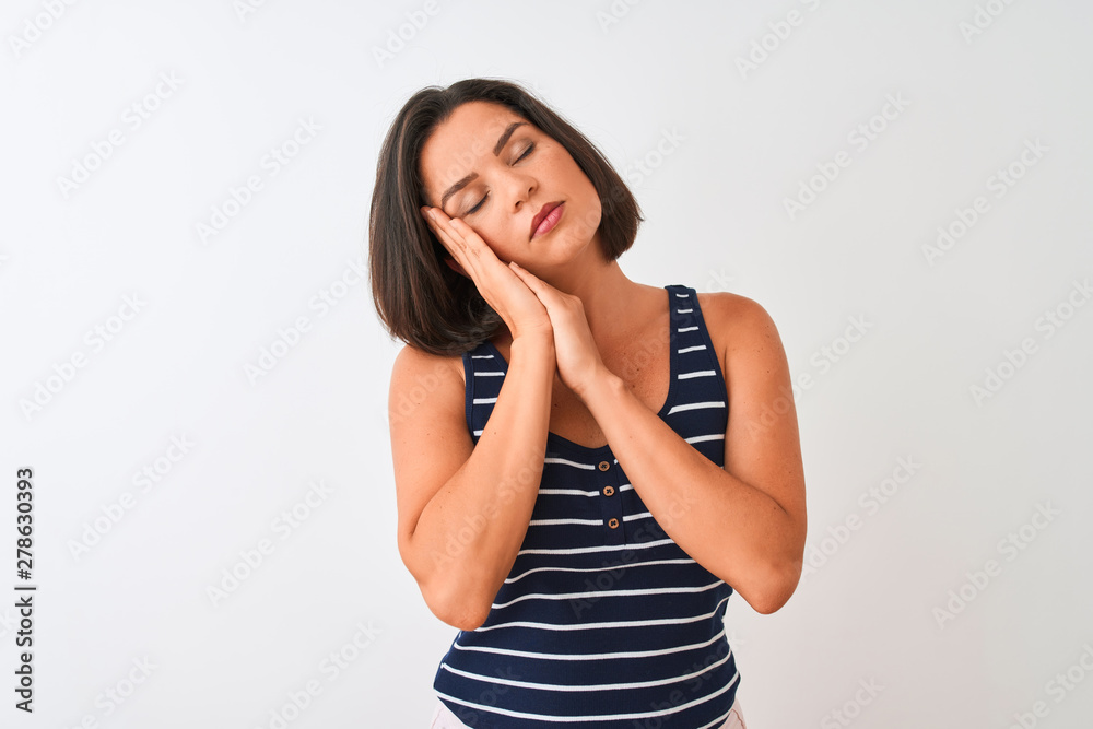 Young beautiful woman wearing blue striped t-shirt standing over isolated white background sleeping tired dreaming and posing with hands together while smiling with closed eyes. Young beautiful woman wearing blue striped t-shirt standing over isolated white background sleeping tired dreaming and posing with hands together while smiling with closed eyes.