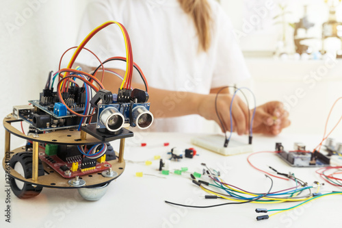 A cute girl constructs metal robot and program it. The boards and microcontrollers are on the table. STEM education inscription. Programming. Mathematics. The science. Technologie. DIY. 