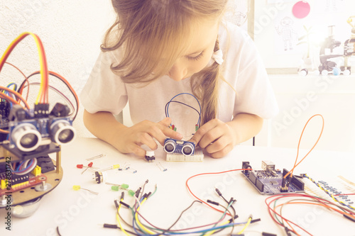 A cute girl constructs metal robot and program it. The boards and microcontrollers are on the table. STEM education inscription. Programming. Mathematics. The science. Technologie. DIY. 