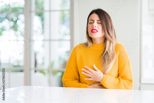 Young beautiful woman wearing winter sweater at home with hand on stomach because nausea, painful disease feeling unwell. Ache concept.