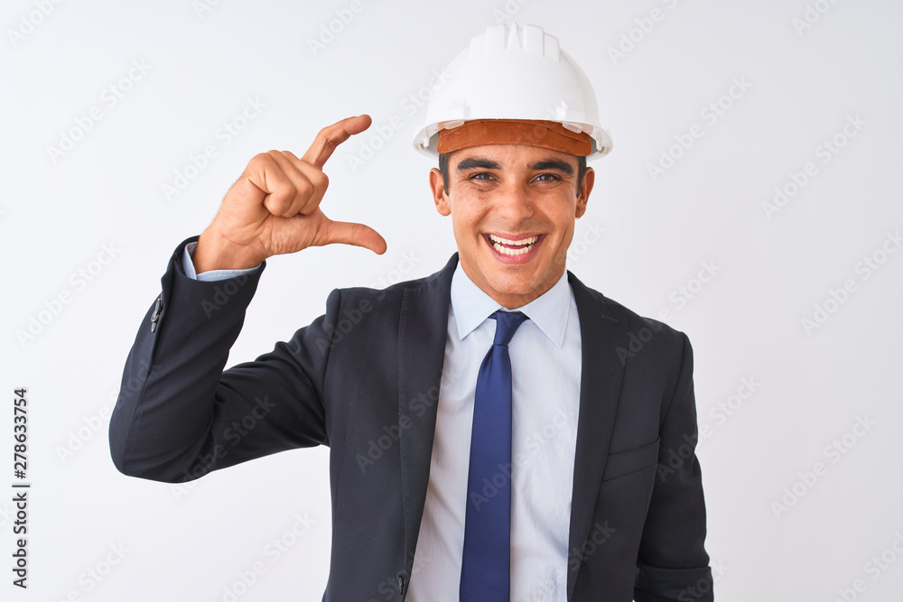 Young handsome architect man wearing suit and helmet over isolated white background smiling and confident gesturing with hand doing small size sign with fingers looking and the camera. 