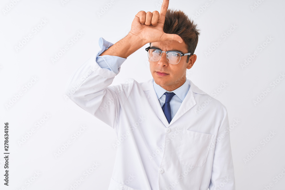 Young handsome sciencist man wearing glasses and coat over isolated white background making fun of people with fingers on forehead doing loser gesture mocking and insulting. Young handsome sciencist man wearing glasses and coat over isolated white background making fun of people with fingers on forehead doing loser gesture mocking and insulting.