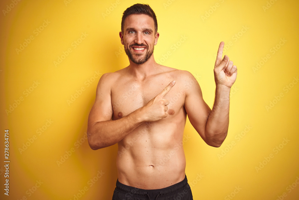 Young handsome shirtless man over isolated yellow background smiling and looking at the camera pointing with two hands and fingers to the side.
