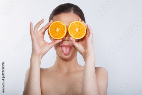 Funny girl holding orange in front of her face and showing tongue.