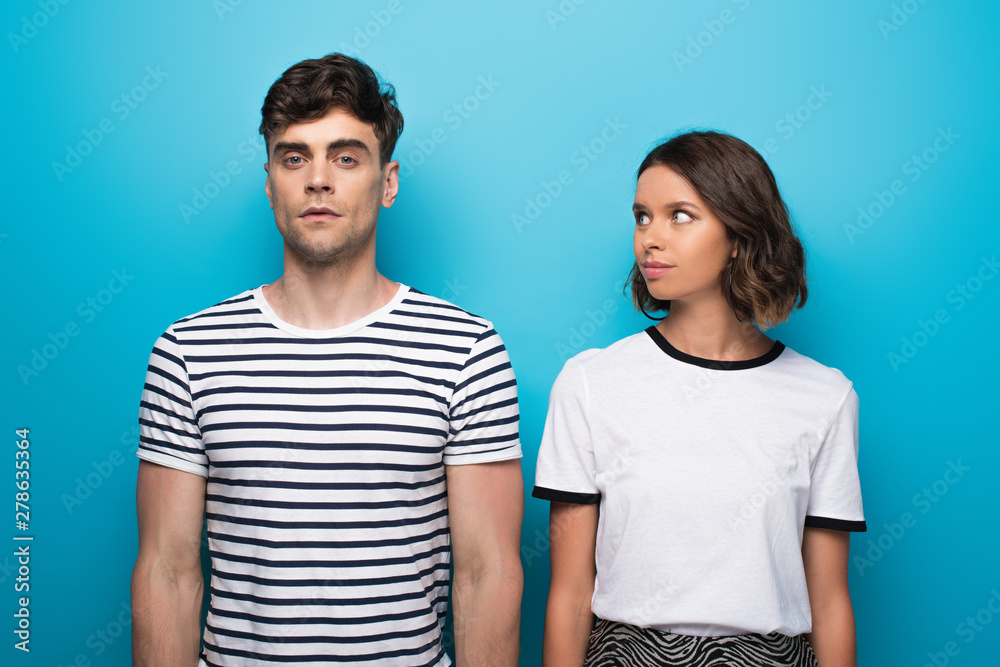 positive young girl looking at offended boyfriend on blue background positive young girl looking at offended boyfriend on blue background