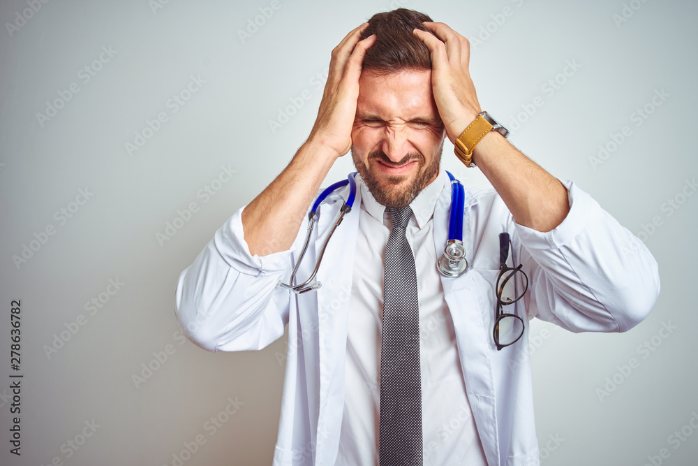 Young handsome doctor man wearing white professional coat over isolated background suffering from headache desperate and stressed because pain and migraine. Hands on head. Young handsome doctor man wearing white professional coat over isolated background suffering from headache desperate and stressed because pain and migraine. Hands on head.