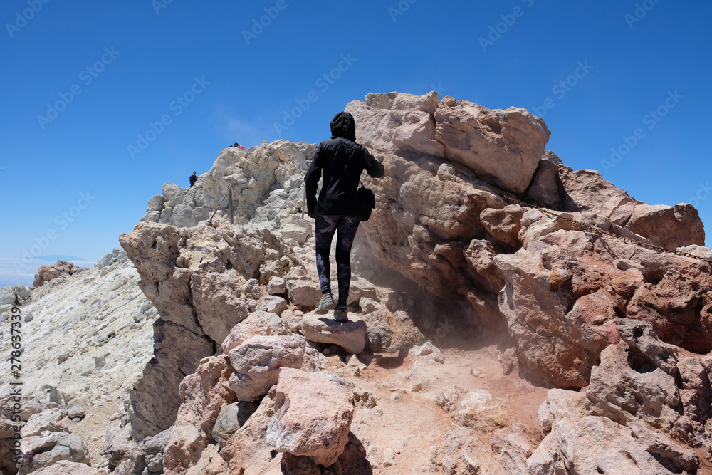 Woman ascending the Teide mountain peak on a dry and rocky volcanic landscape