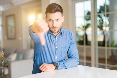 Young handsome man at home with angry face, negative sign showing dislike with thumbs down, rejection concept