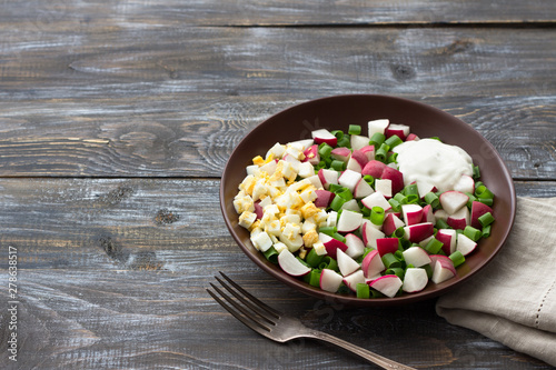 Fresh radish salad with green onions, boiled egg and sour cream on a wooden background, rustic style. Delicious homemade food
