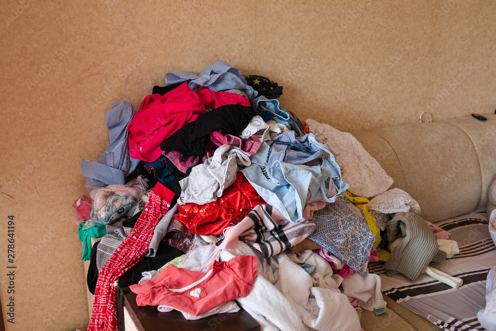 Front view of colorful childish clothes scattered on sofa at home. Big bunch of clothes lying at room before laundry. Concept of cleaning, mess, mud and household chores.