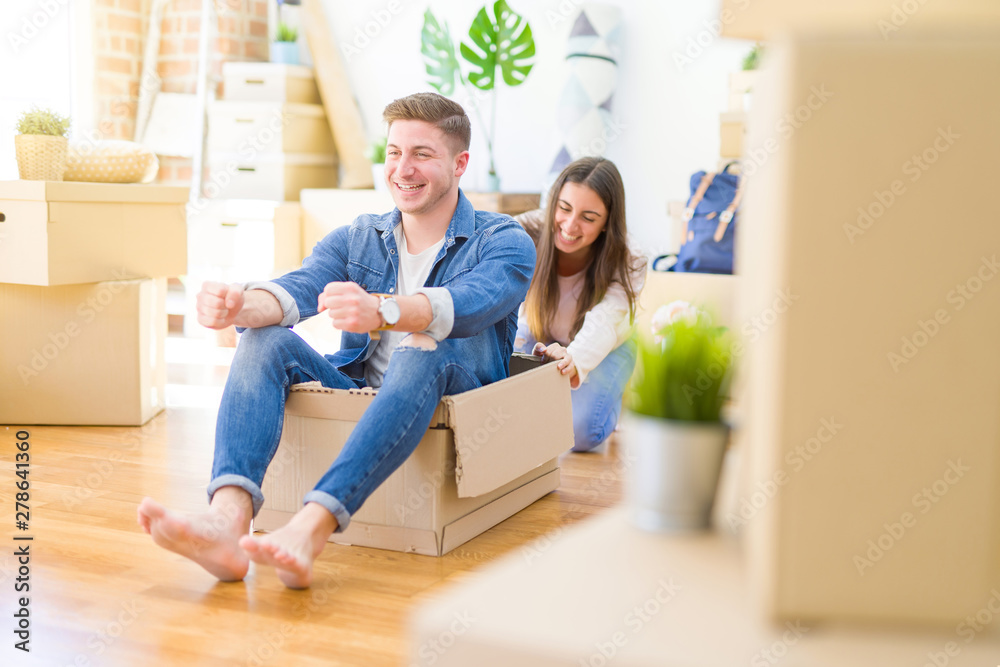 Beautiful young couple smiling in love having fun riding inside a cardboard box, celebrating moving to a new home Beautiful young couple smiling in love having fun riding inside a cardboard box, celebrating moving to a new home