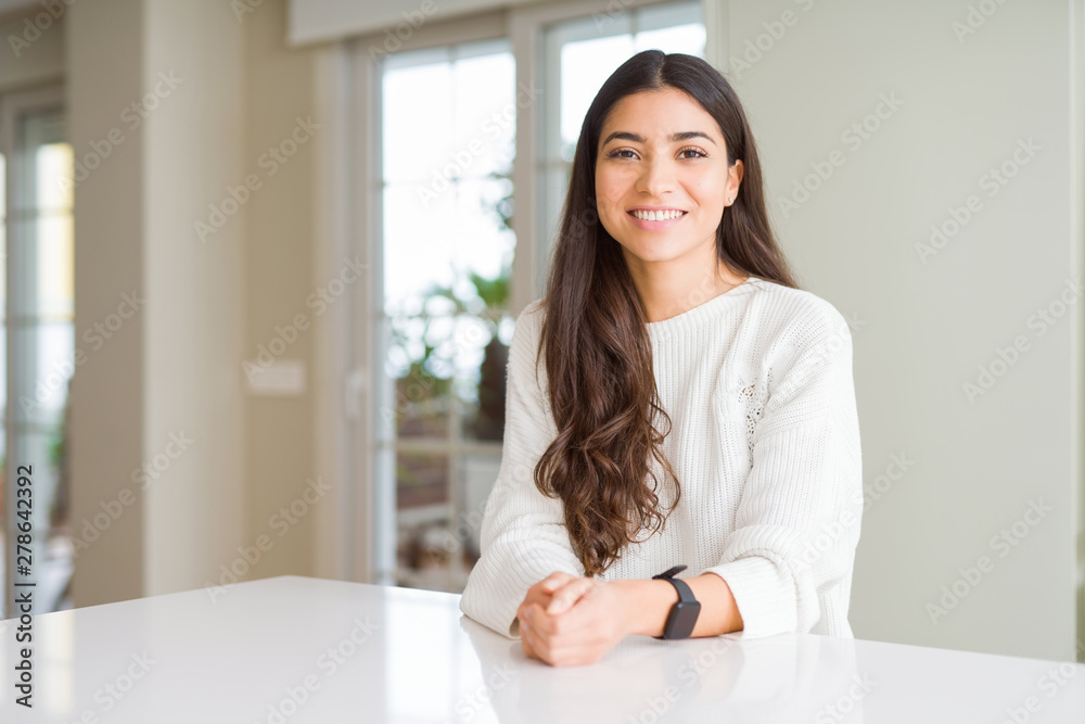 Young beautiful woman at home on white table with a happy and cool smile on face. Lucky person.