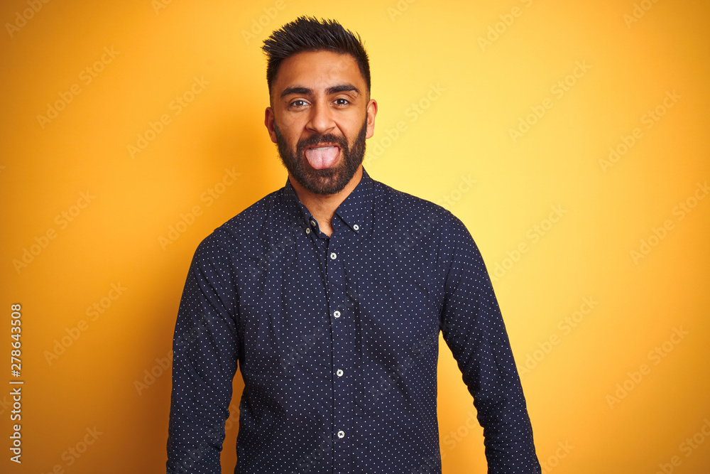 Fototapeta premium Young handsome indian businessman wearing shirt over isolated yellow background sticking tongue out happy with funny expression. Emotion concept.