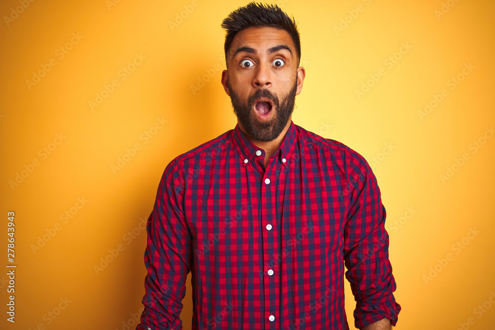 Obraz premium Young indian man wearing casual shirt standing over isolated yellow background afraid and shocked with surprise expression, fear and excited face.