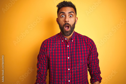 Young indian man wearing casual shirt standing over isolated yellow background afraid and shocked with surprise expression, fear and excited face.