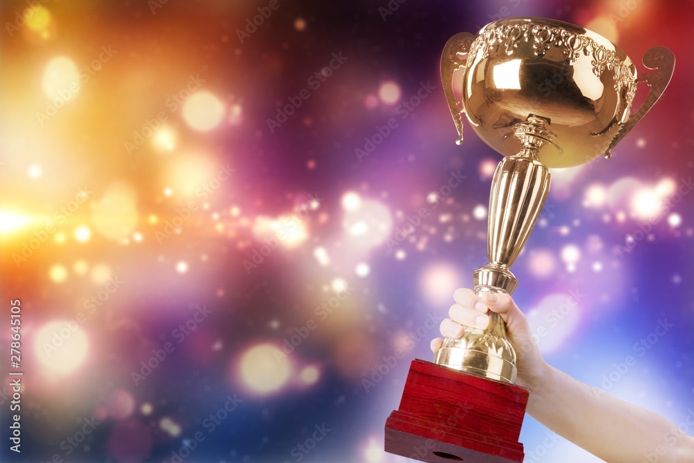 Fototapeta premium Close-up human hand holding golden Trophy on blurred blue background