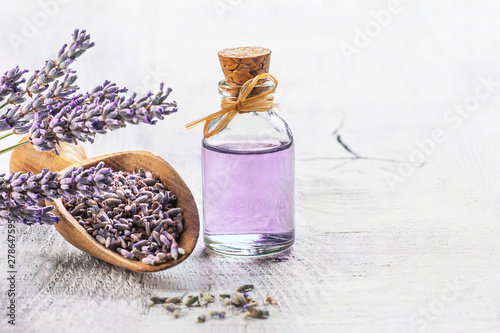 Glass bottle of Lavender essential oil with fresh lavender flowers and dried lavender seeds on white wooden rustic table, aromatherapy spa massage concept. Lavendula oleum