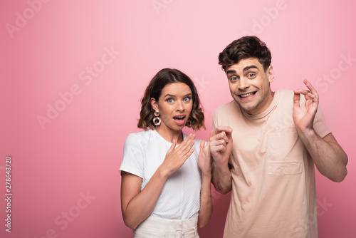 emotional man and woman gesturing shut up while looking at camera on pink background