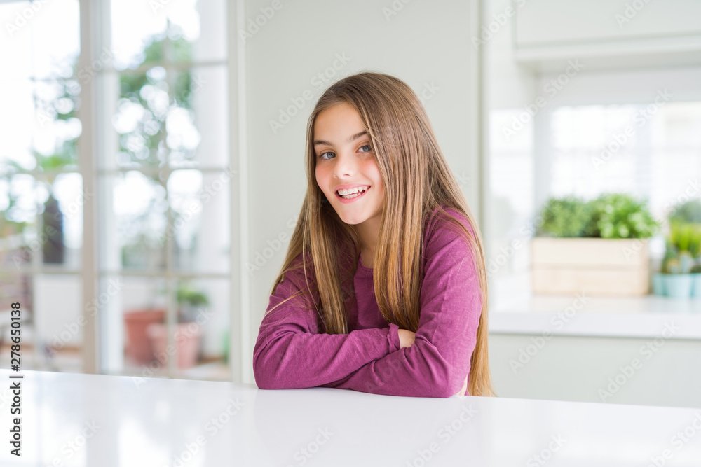 Beautiful young girl kid on white table happy face smiling with crossed arms looking at the camera. Positive person.