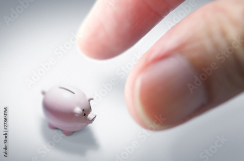 Inflation vs Savings, illustrated by tiny piggy bank (diminishing value of savings) compared to fingers. photo