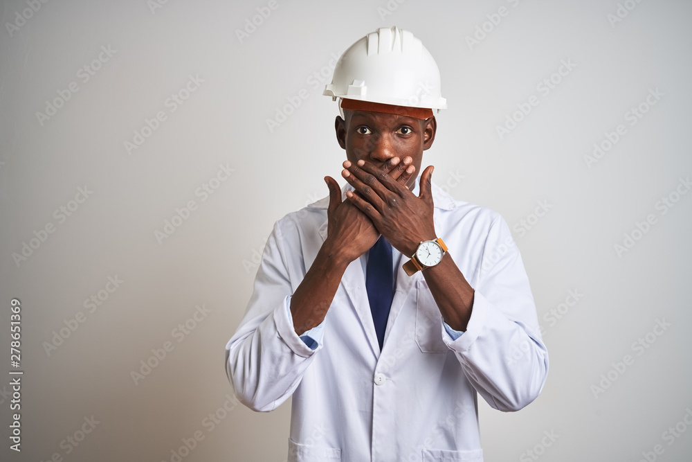 African american engineer man wearing coat and helmet over isolated white background shocked covering mouth with hands for mistake. Secret concept. African american engineer man wearing coat and helmet over isolated white background shocked covering mouth with hands for mistake. Secret concept.