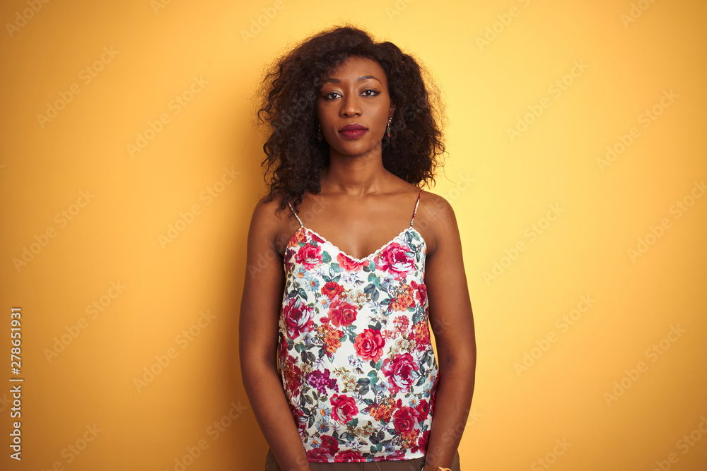 African american woman wearing floral summer t-shirt over isolated yellow background Relaxed with serious expression on face. Simple and natural looking at the camera. African american woman wearing floral summer t-shirt over isolated yellow background Relaxed with serious expression on face. Simple and natural looking at the camera.