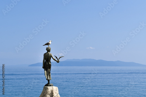Living seagull standing on top of sculpture named Girl with a seagull