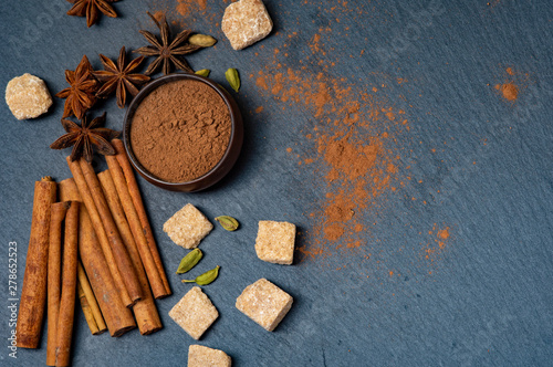 Brown star anise and cinnamon on a dark background. Ground cinnamon in a cup. Cardamom and cane sugar.