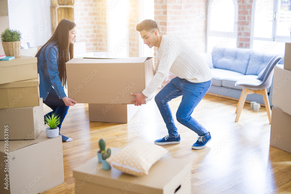 Beautiful young asian couple looking happy, holding a big cardboard box smiling excited moving to a new home