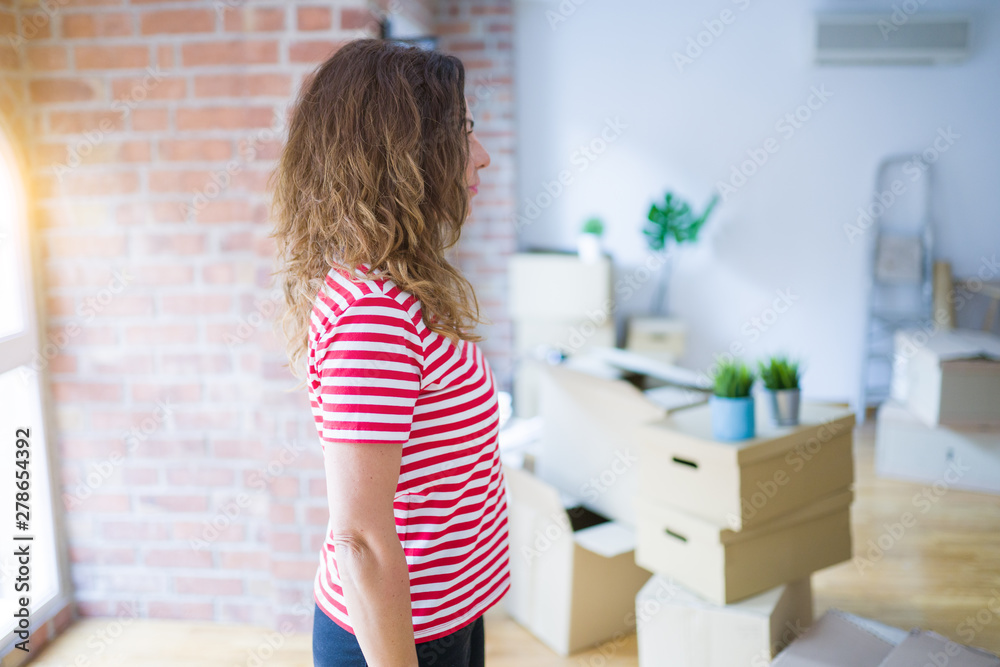 Middle age senior woman moving to a new house packing cardboard boxes looking to side, relax profile pose with natural face with confident smile.
