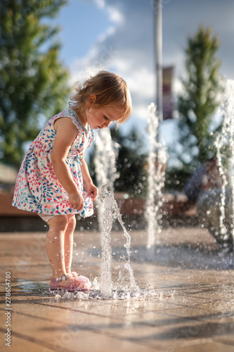 Little Girl Playing with Splash Fountain in Colorful Dress