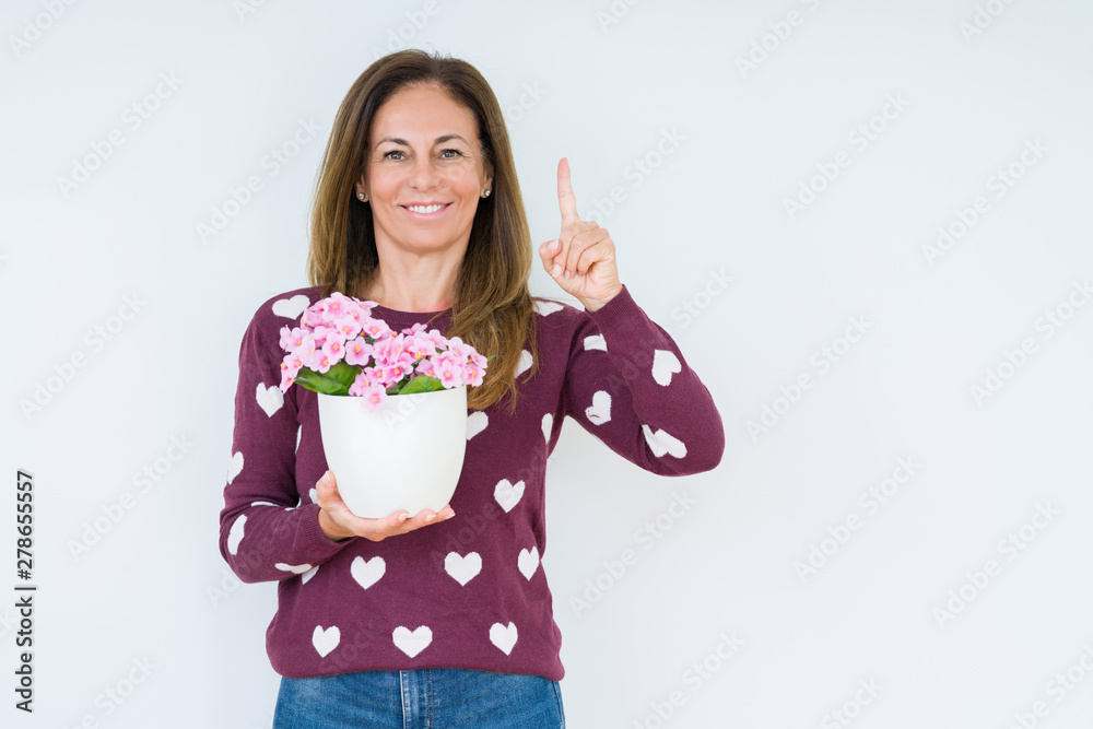 Middle age woman holding flowers pot plant over isolated background surprised with an idea or question pointing finger with happy face, number one Middle age woman holding flowers pot plant over isolated background surprised with an idea or question pointing finger with happy face, number one