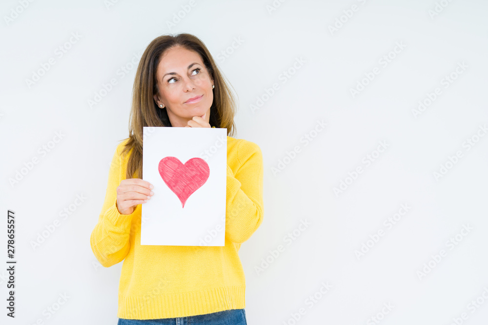 Middle age woman holding card gift with red heart over isolated background serious face thinking about question, very confused idea Middle age woman holding card gift with red heart over isolated background serious face thinking about question, very confused idea