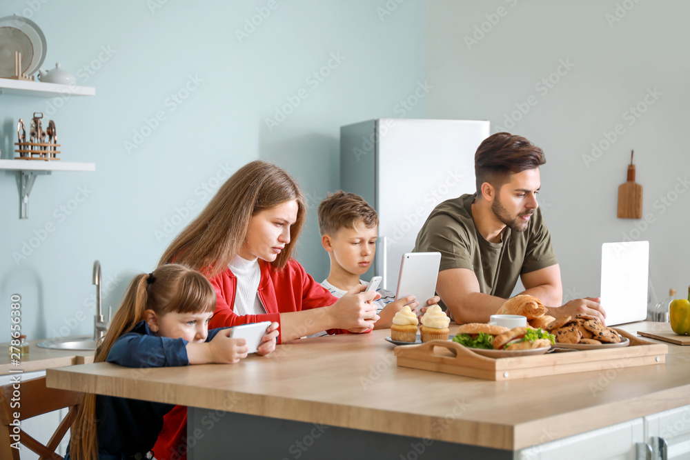 Family with addiction to modern technologies sitting at table in kitchen Family with addiction to modern technologies sitting at table in kitchen