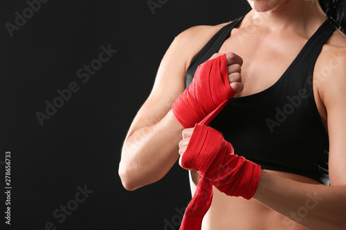 Sporty female boxer applying wrist bands against dark background © Pixel-Shot