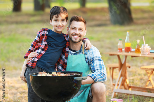 Little boy with father cooking tasty food on barbecue grill outdoors