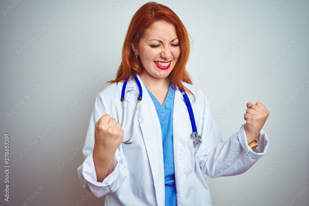 Young redhead doctor woman using stethoscope over white isolated background very happy and excited doing winner gesture with arms raised, smiling and screaming for success. Celebration concept.