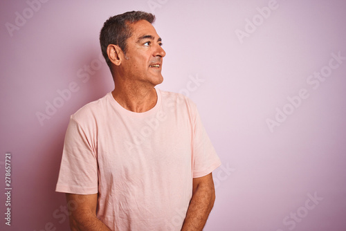 Handsome middle age man wearing t-shirt standing over isolated pink background looking away to side with smile on face, natural expression. Laughing confident.