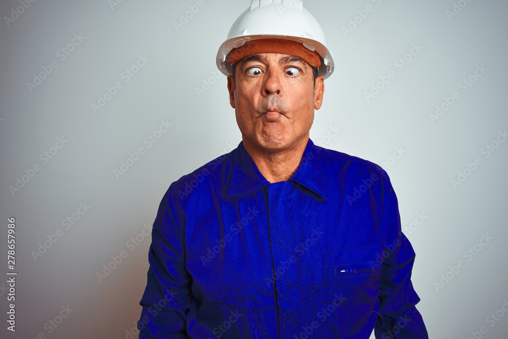 Handsome middle age worker man wearing uniform and helmet over isolated white background making fish face with lips, crazy and comical gesture. Funny expression. Handsome middle age worker man wearing uniform and helmet over isolated white background making fish face with lips, crazy and comical gesture. Funny expression.