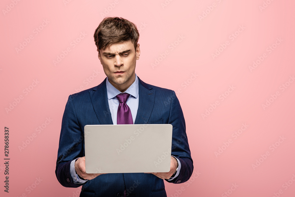 thoughtful businessman in suit standing with laptop on pink background thoughtful businessman in suit standing with laptop on pink background