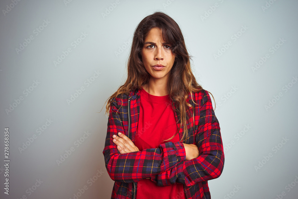 Young beautiful woman wearing red t-shirt and jacket standing over white isolated background skeptic and nervous, disapproving expression on face with crossed arms. Negative person. Young beautiful woman wearing red t-shirt and jacket standing over white isolated background skeptic and nervous, disapproving expression on face with crossed arms. Negative person.