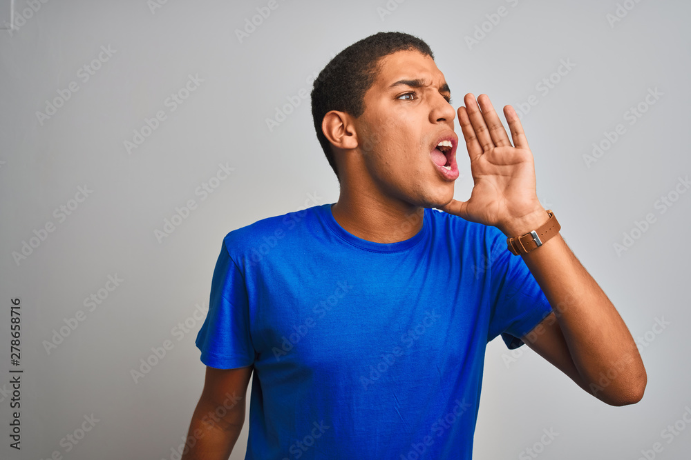 Young handsome arab man wearing blue t-shirt standing over isolated white background shouting and screaming loud to side with hand on mouth. Communication concept. Young handsome arab man wearing blue t-shirt standing over isolated white background shouting and screaming loud to side with hand on mouth. Communication concept.
