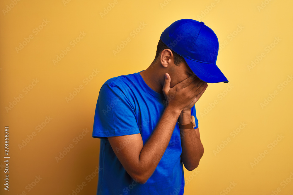 Young handsome arab delivery man standing over isolated yellow background with sad expression covering face with hands while crying. Depression concept.