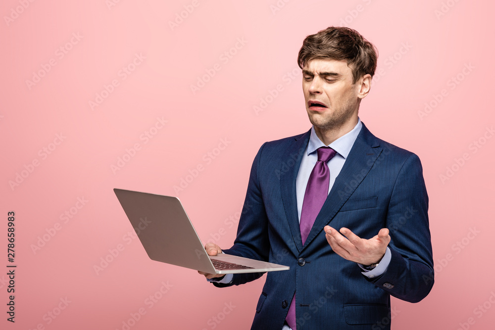 displeased businessman gesturing while looking at laptop on pink background displeased businessman gesturing while looking at laptop on pink background