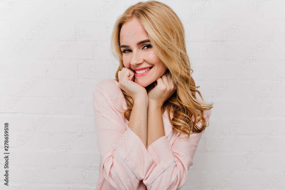 Pleasant young woman with trendy hairstyle smiling on white background. Blissful pale girl in pink pyjamas posing early in morning at home. Pleasant young woman with trendy hairstyle smiling on white background. Blissful pale girl in pink pyjamas posing early in morning at home.