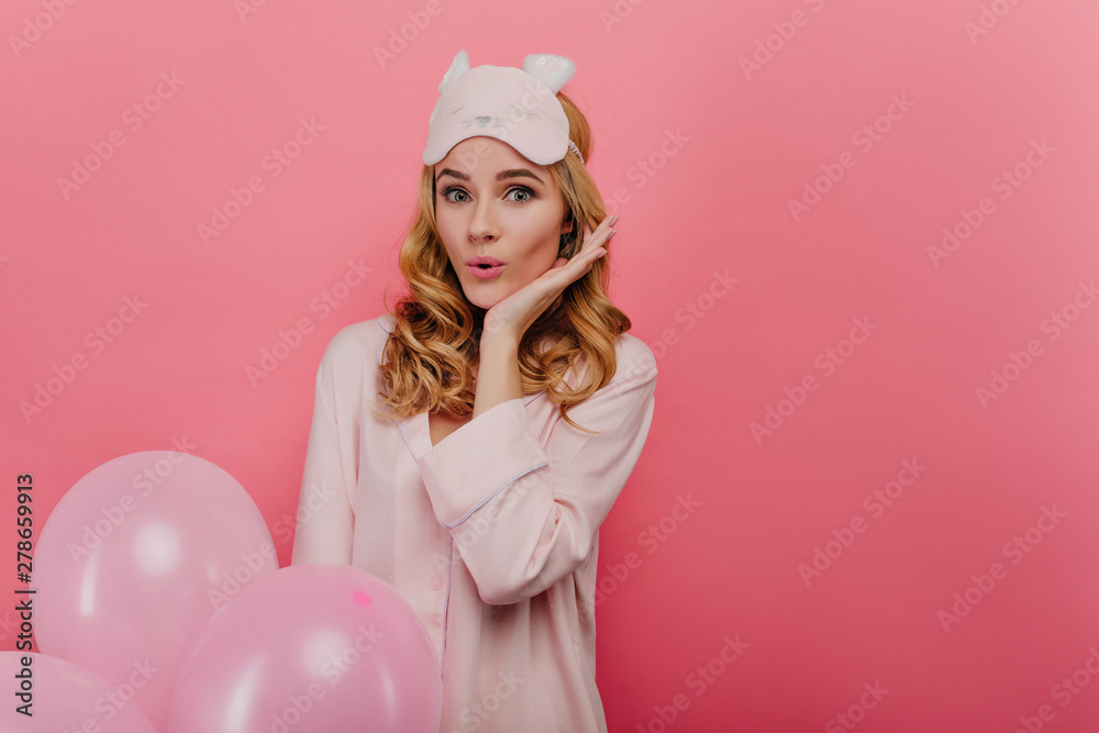 Surprised glamorous woman with wavy hairstyle enjoying birthday in morning. Good-looking girl in eyemask and pyjama holding pink balloons. Surprised glamorous woman with wavy hairstyle enjoying birthday in morning. Good-looking girl in eyemask and pyjama holding pink balloons.