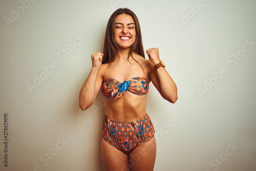 Young beautiful woman on vacation wearing bikini standing over isolated white background excited for success with arms raised and eyes closed celebrating victory smiling. Winner concept.