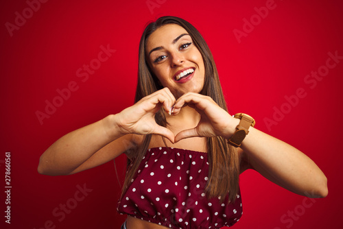 Young beautiful woman wearing casual t-shirt standing over isolated red background smiling in love showing heart symbol and shape with hands. Romantic concept.