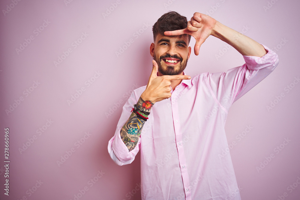 Young man with tattoo wearing shirt standing over isolated pink background smiling making frame with hands and fingers with happy face. Creativity and photography concept. Young man with tattoo wearing shirt standing over isolated pink background smiling making frame with hands and fingers with happy face. Creativity and photography concept.